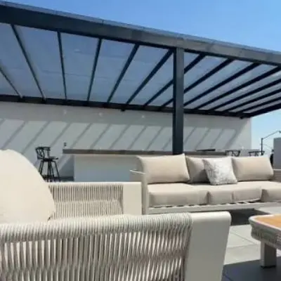 Terraza soleada con sillón de mimbre, sofá y pérgola con sombra