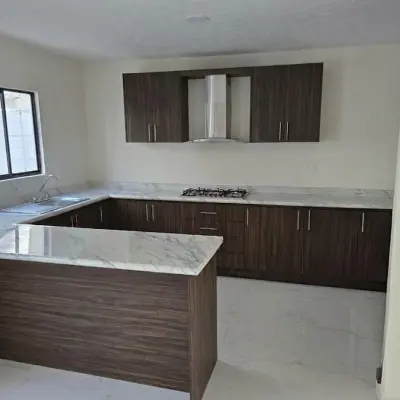 Cocina integral terminada: alacenas de madera, cubierta clara, parrilla empotrada, campana de acero, tarja junto a la ventana e isla al frente